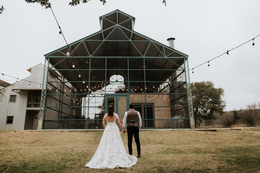 A wedding couple hold hands while standing in front of an empty building frame.