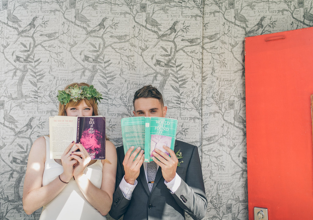Two people hold books up to their faces, books with wedding readings in them.