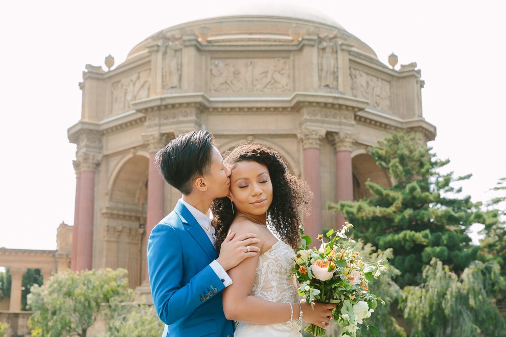A wedding couple stand close in front of a grand arch