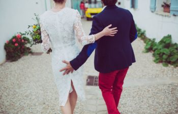 A wedding couple walk along as one person grabs the other person's buttocks.