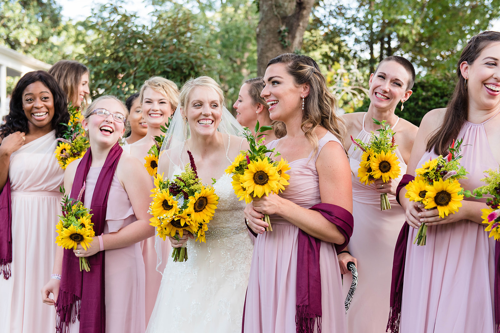 A bridal party stand and laugh wearing pink and blush bridesmaid dresses