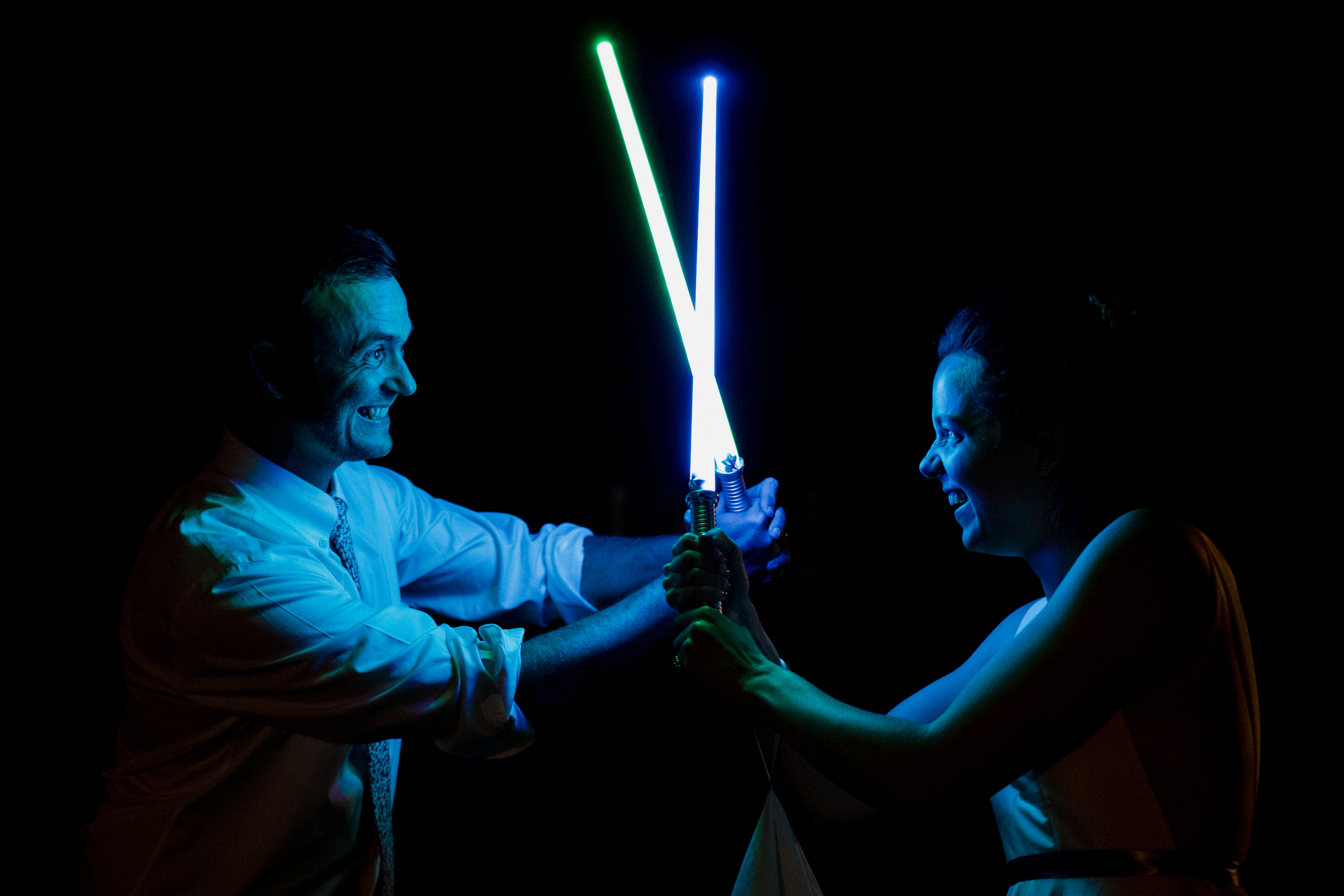 A wedding couple smile as they have a light saber battle