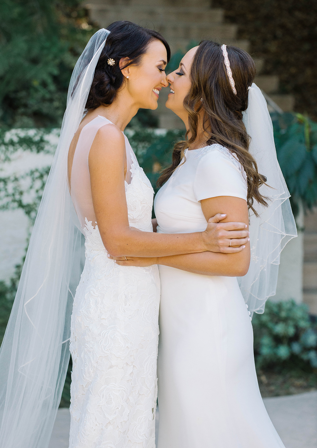 Two women in wedding dresses embrace.