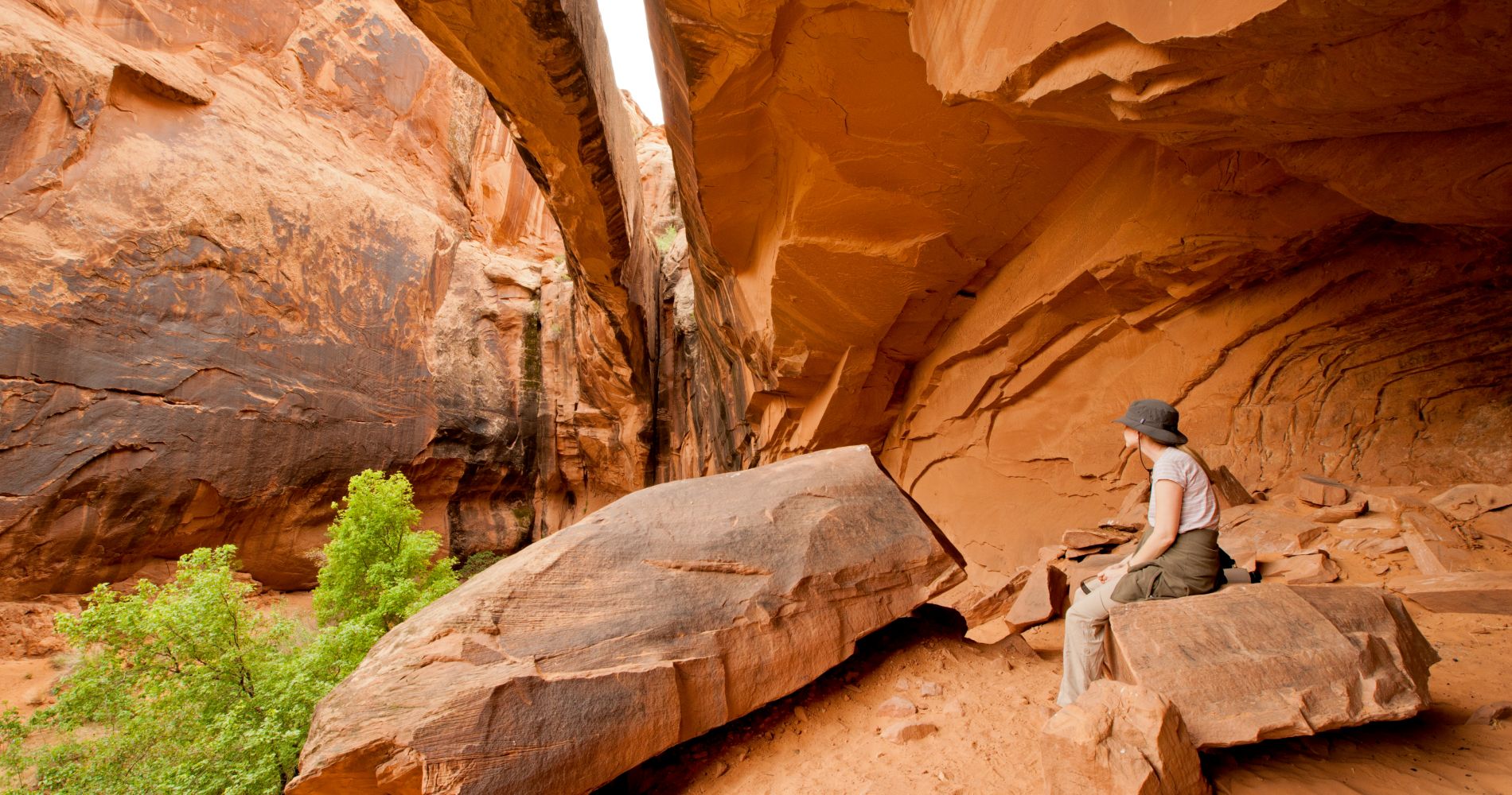 a person sits in a cave in Utah, looking out at the side of a large cliff