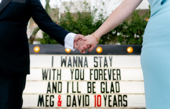 Couple holding hands in front of marquee sign at The Ace Hotel Palm Springs