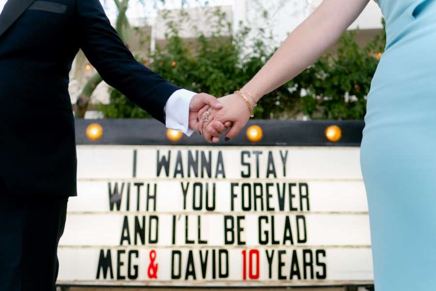 Couple holding hands in front of marquee sign at The Ace Hotel Palm Springs