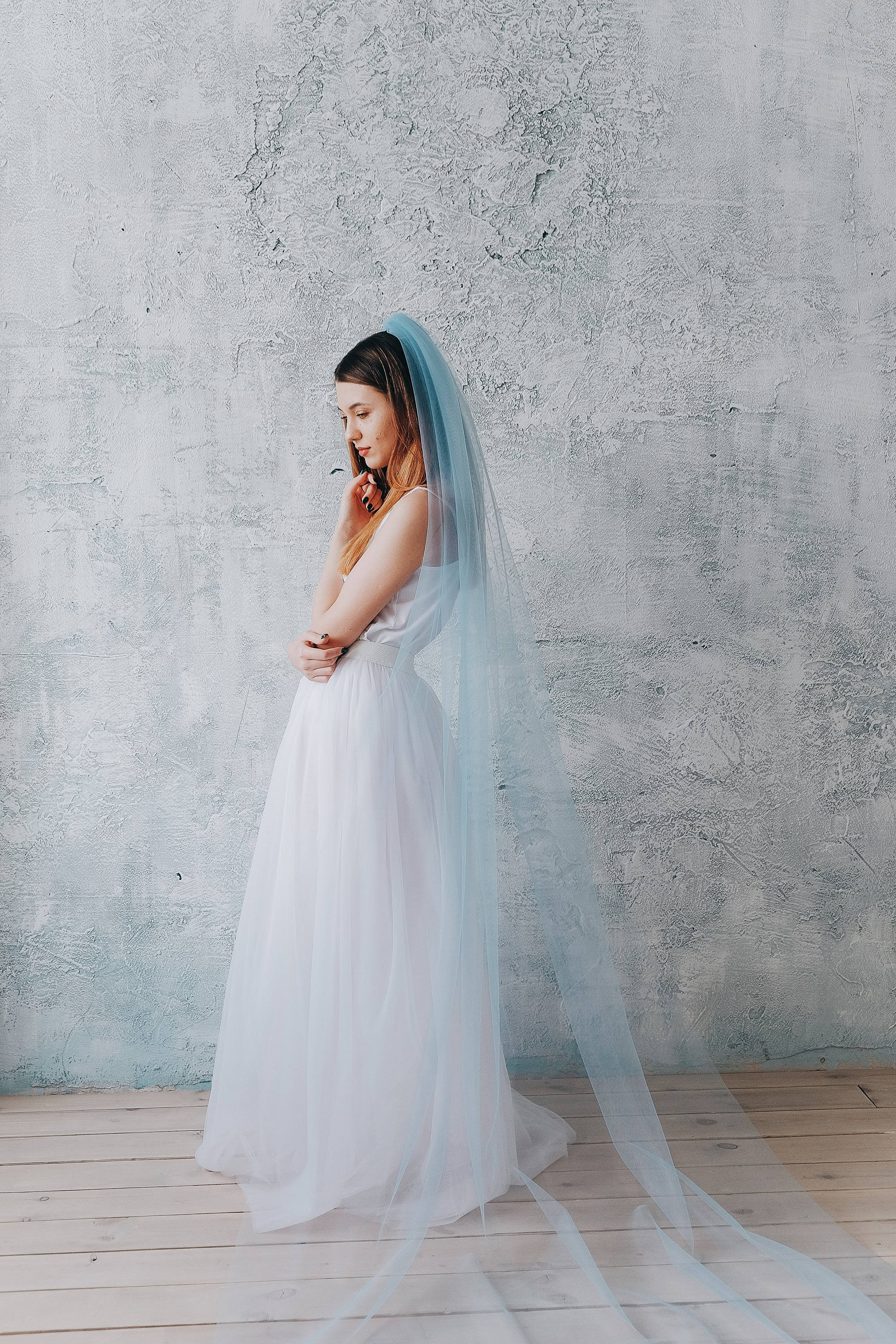 A woman wears a wedding dress in front of a grey concrete wall.