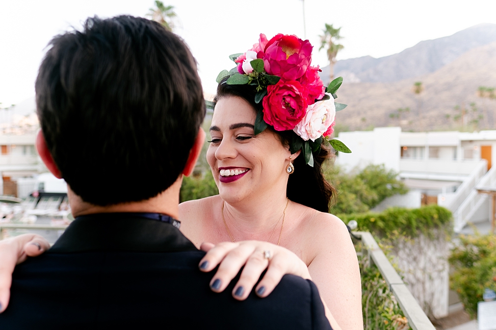 Man and woman embrace, woman wears large pink fake wedding flower headpiece