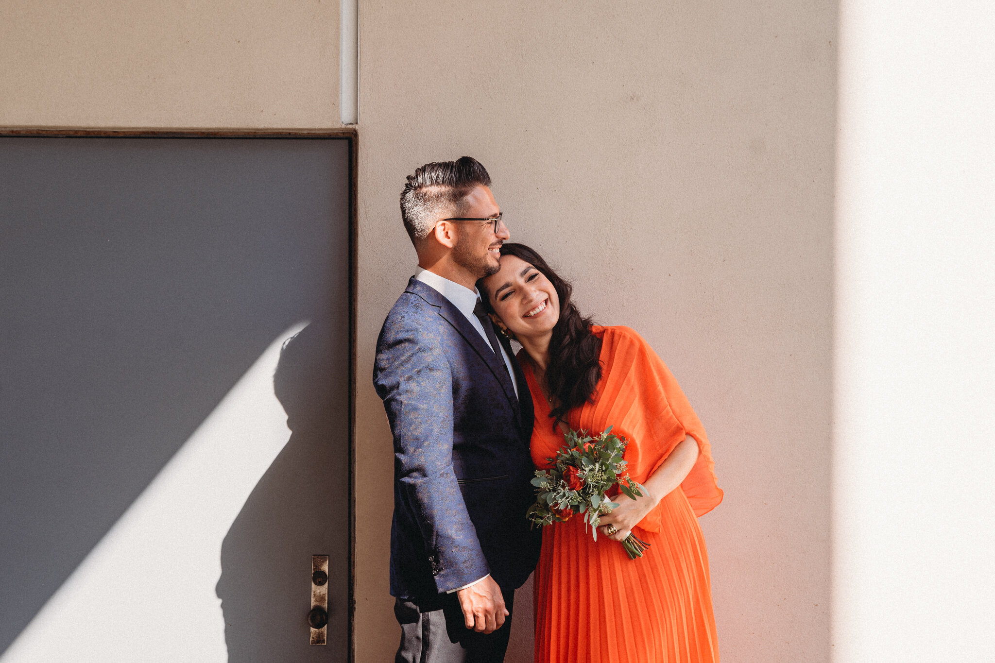 A wedding couple stand in shadow and smile together.