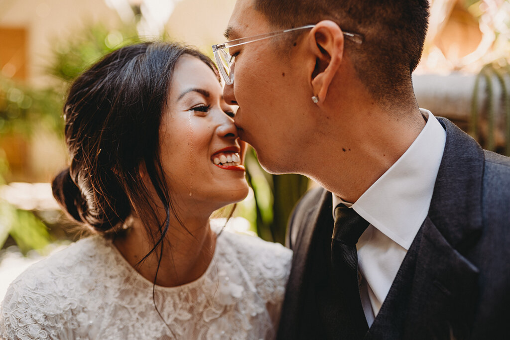A person gently kisses another person's nose on their wedding day.