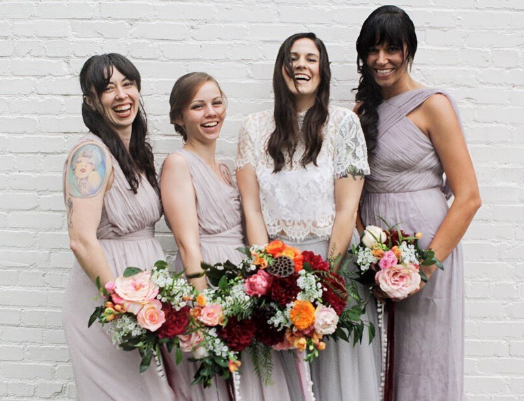 bride and three bridesmaids laughing holding bouquets made of multicolor fake wedding flowers
