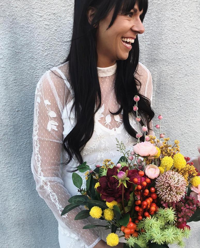 woman in white lace dress holds fake wedding flower bouquet in multiple colors
