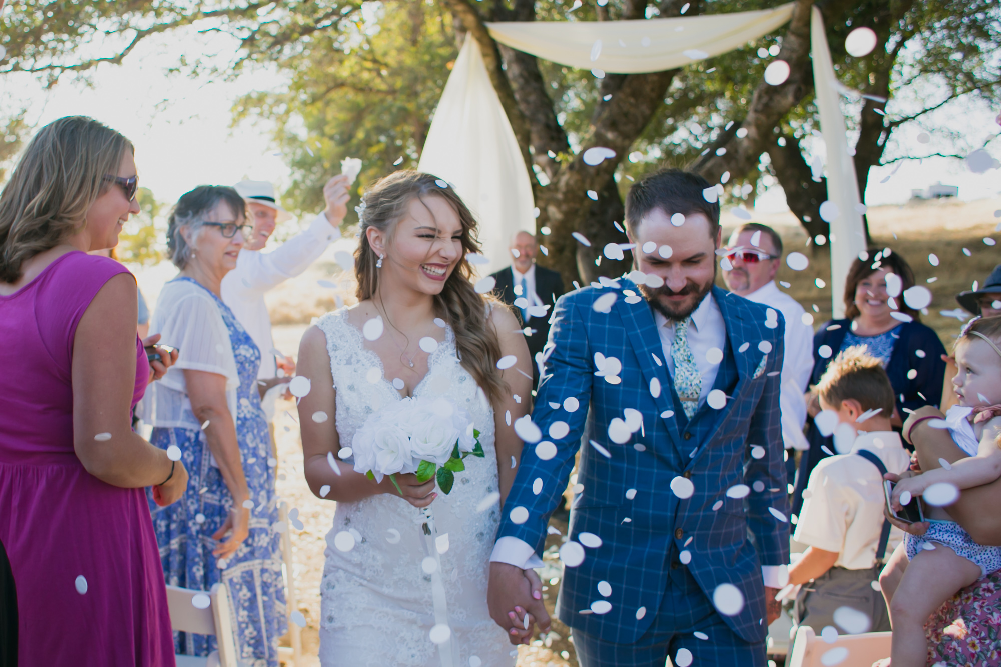 A wedding couple exit their wedding ceremony as people throw confetti along the pathway.