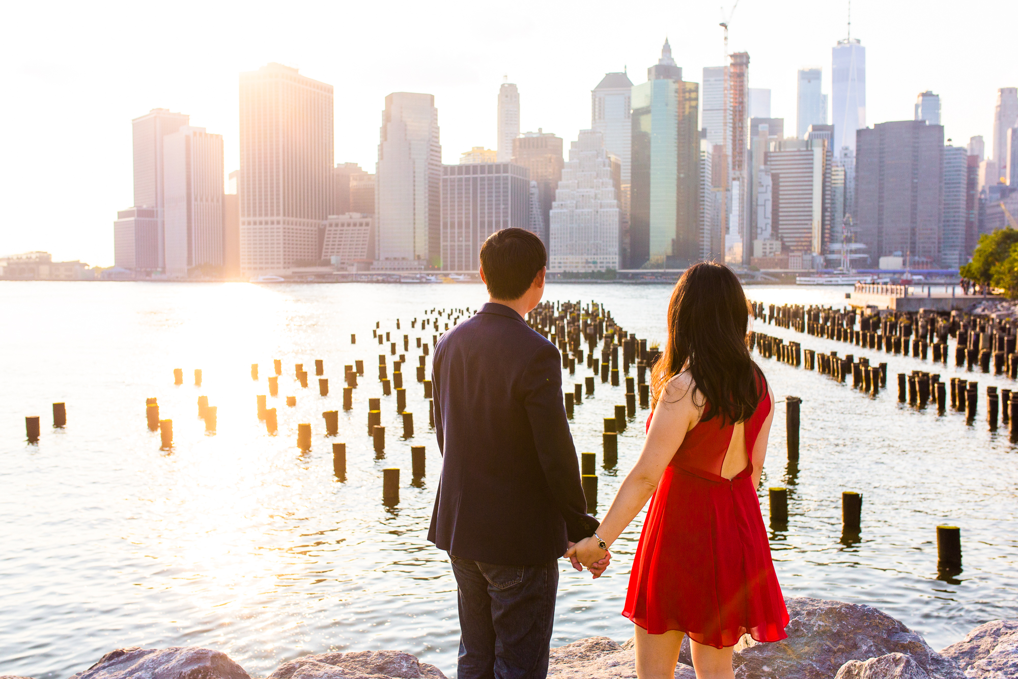 Two people holding hands look out across a bay towards the city.
