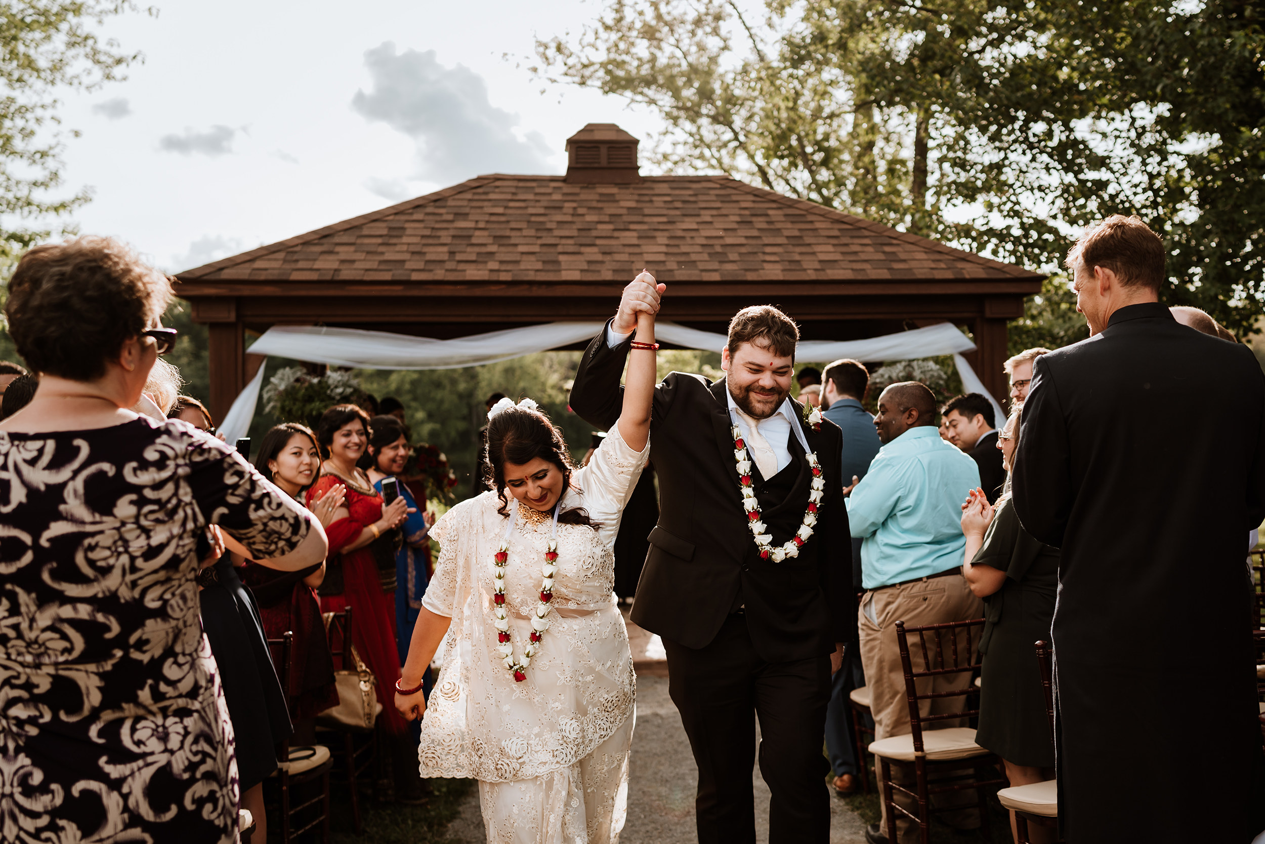 A wedding couple hold hands and raise them in the air as they exit their wedding ceremony.