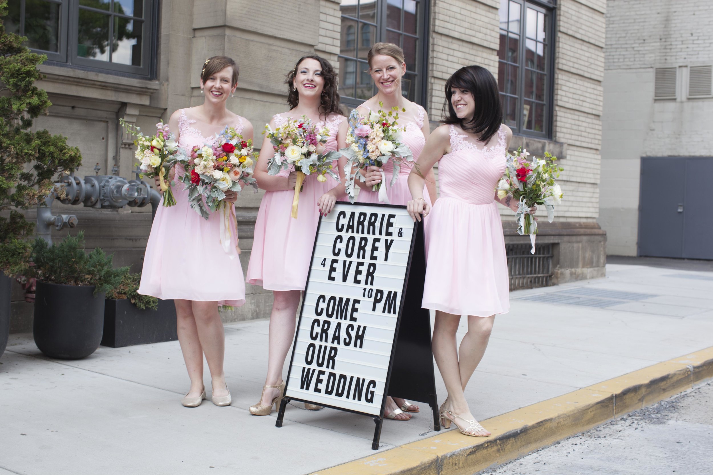 Four bridesmaids stand on a sidewalk.