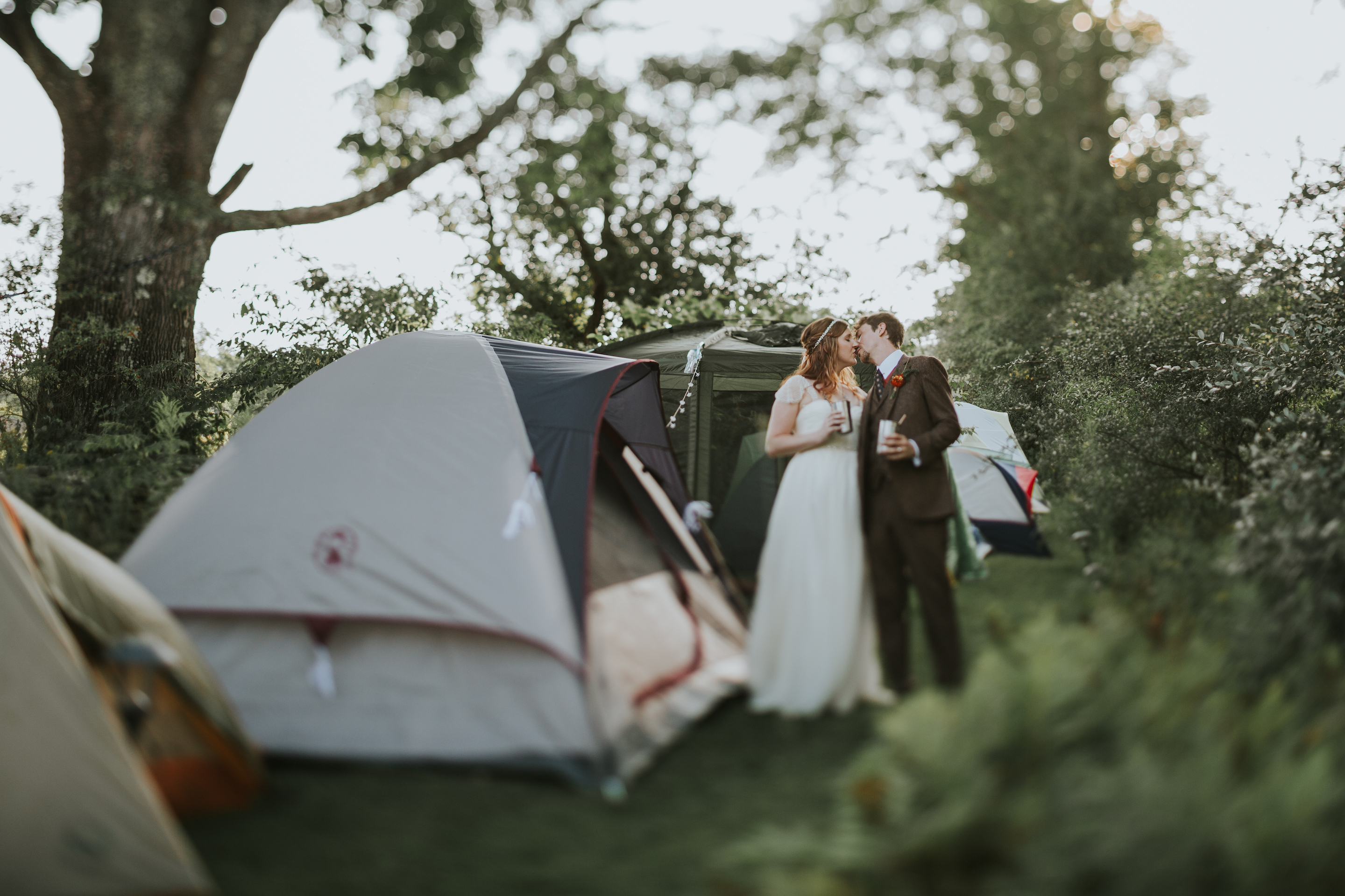 A couple kiss on their wedding day while surrounded by camping tents.