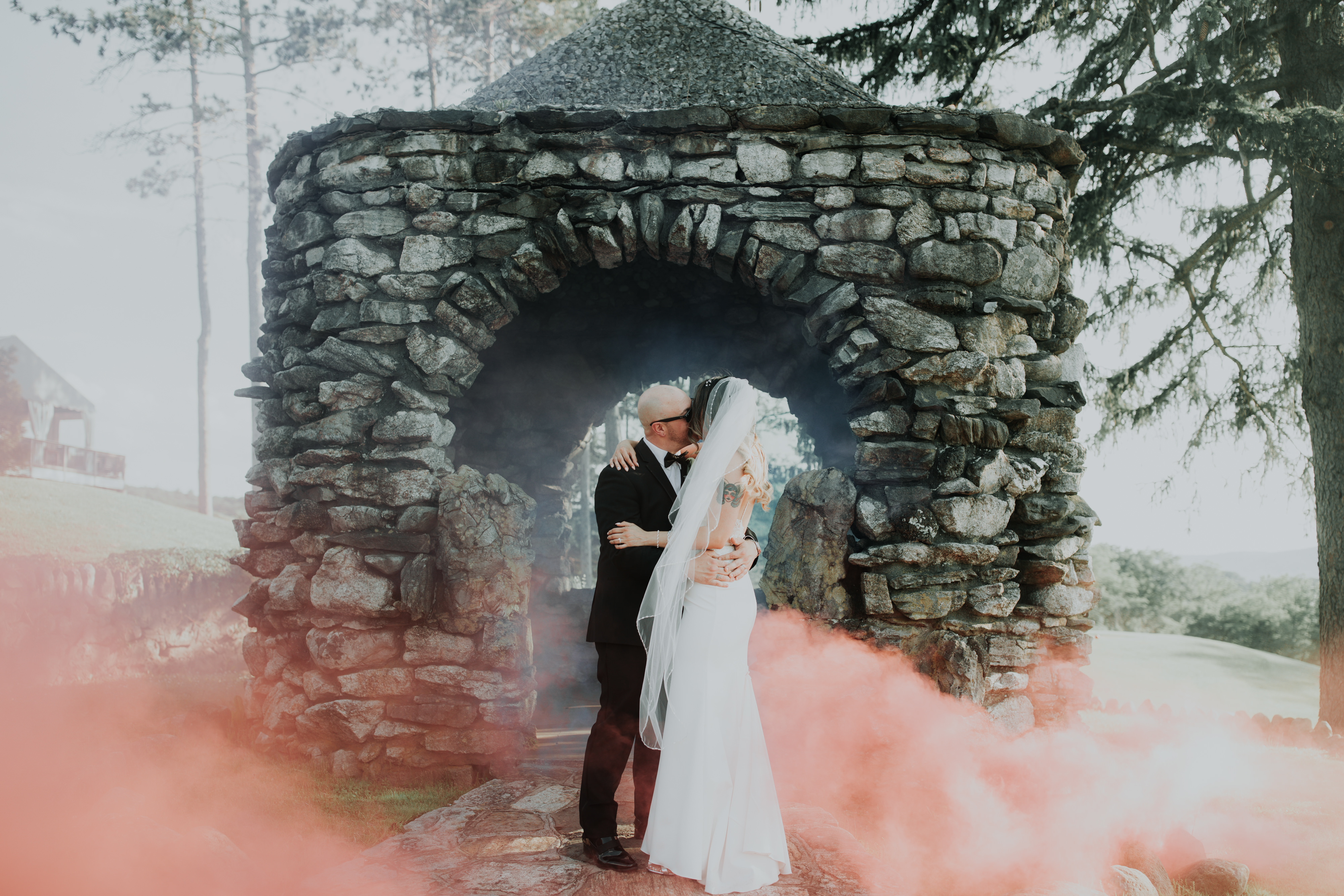 A man and woman embrace while pink smoke floats around them.