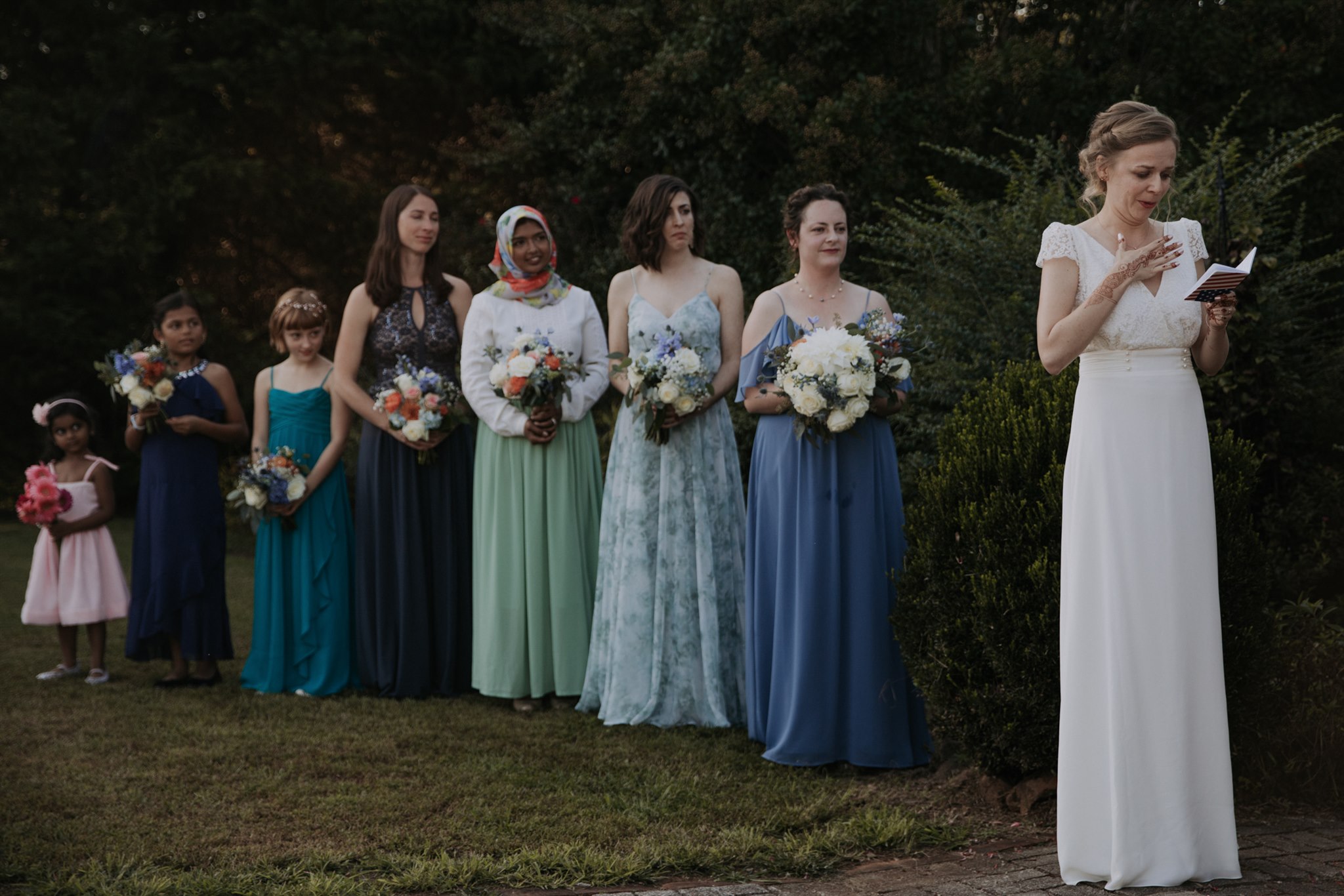 A bride reads her vows while her brides-persons stand in line behind her.