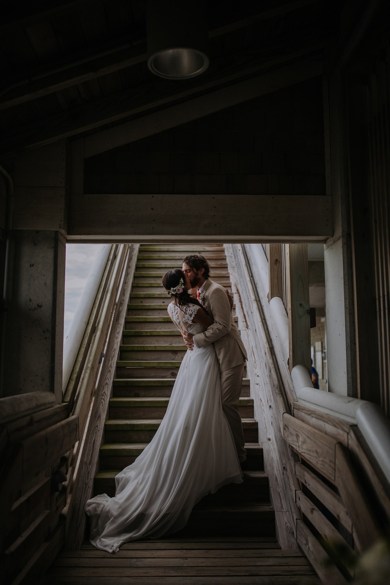 A wedding couple kiss at the bottom of a staircase.