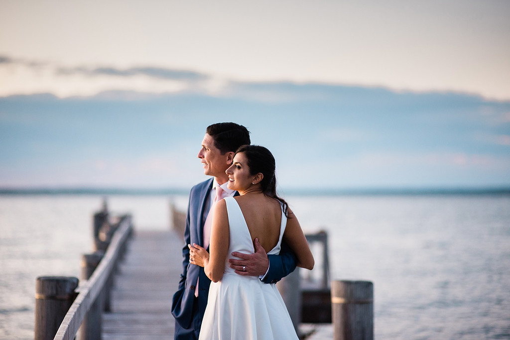 A man and woman stand on a dock at sunset.