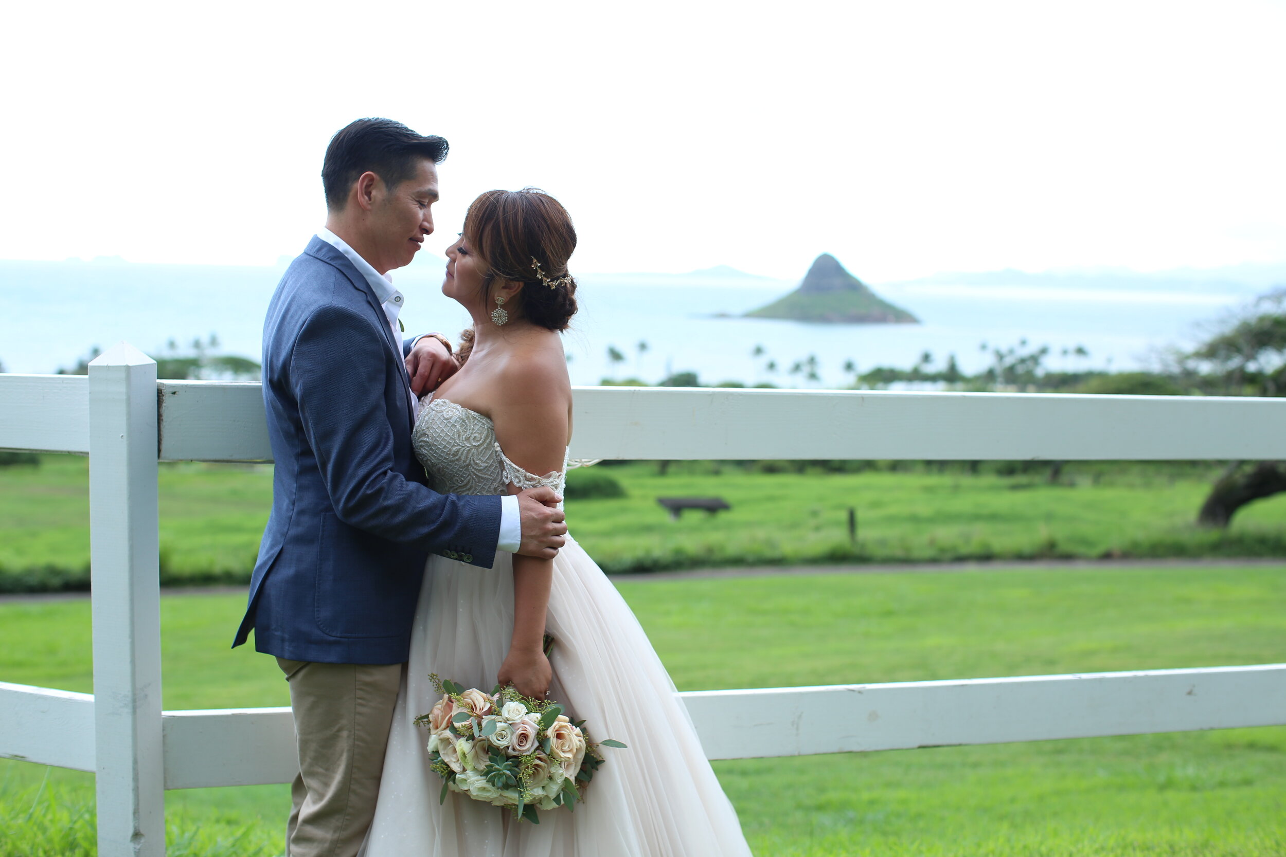 A wedding couple pose for a photo in Hawaii with the Chinaman's hat in the background.