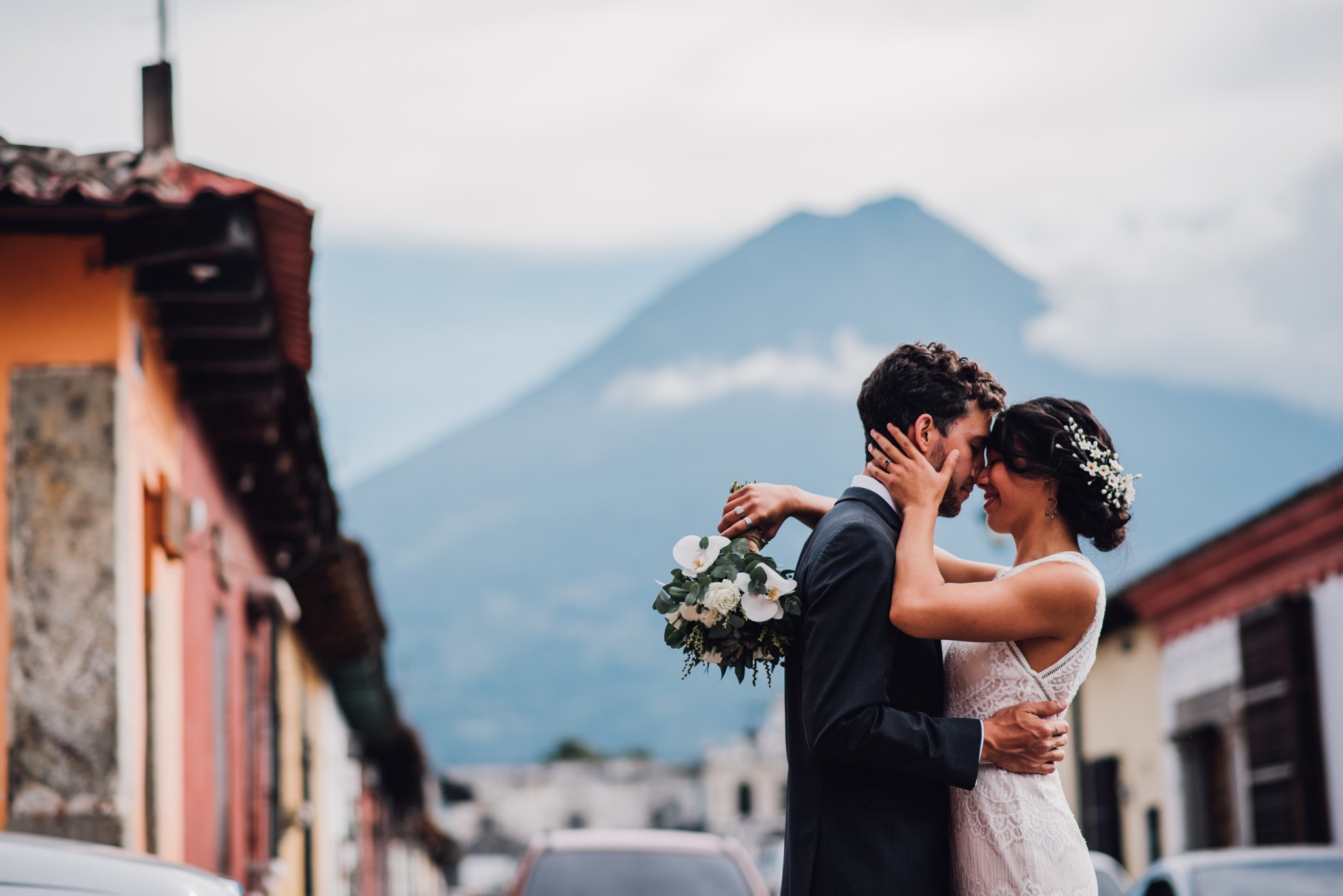 A wedding couple embrace in the shadow of a volcano