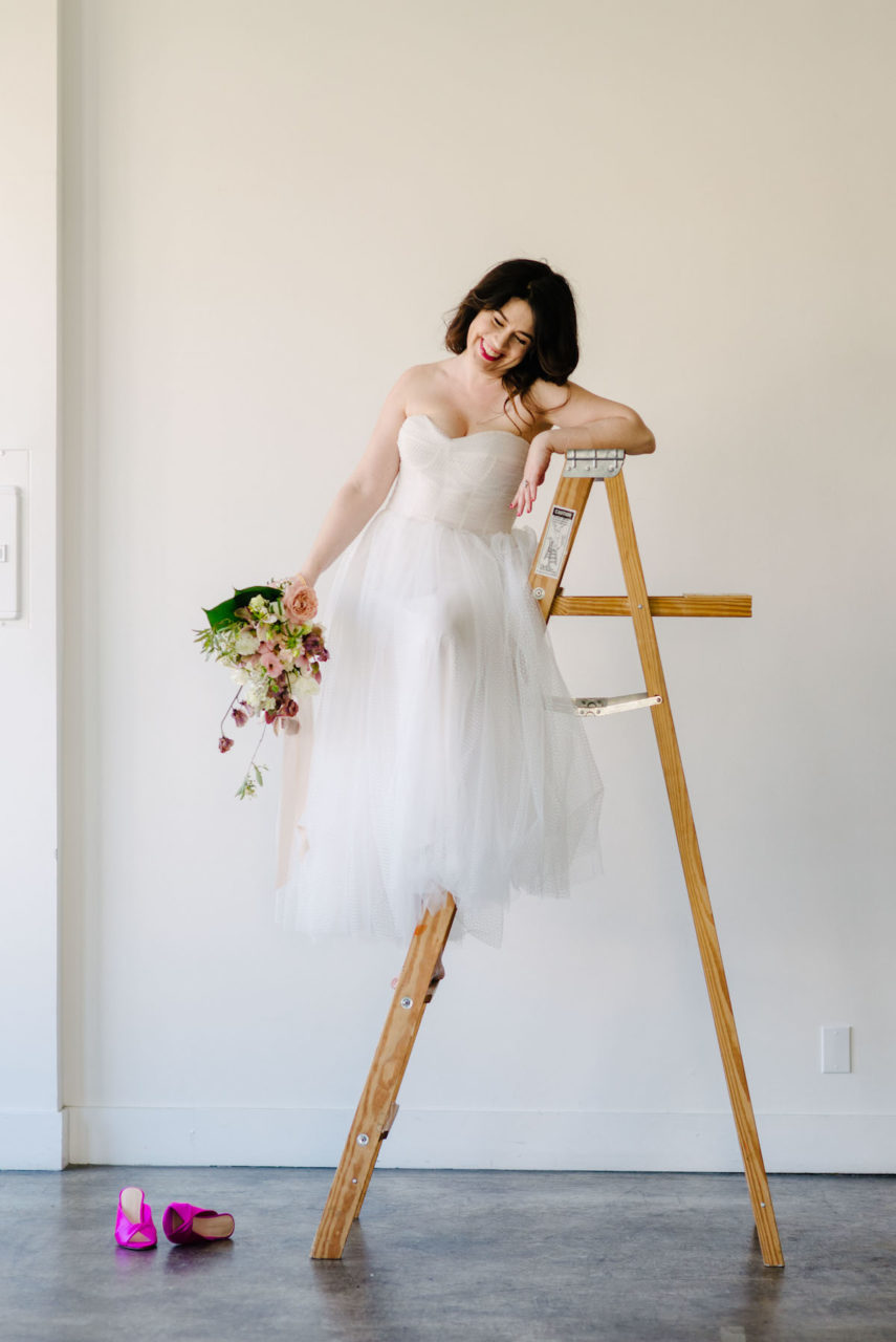 Meg standing on a ladder while wearing a wedding dress and holding a bouquet.