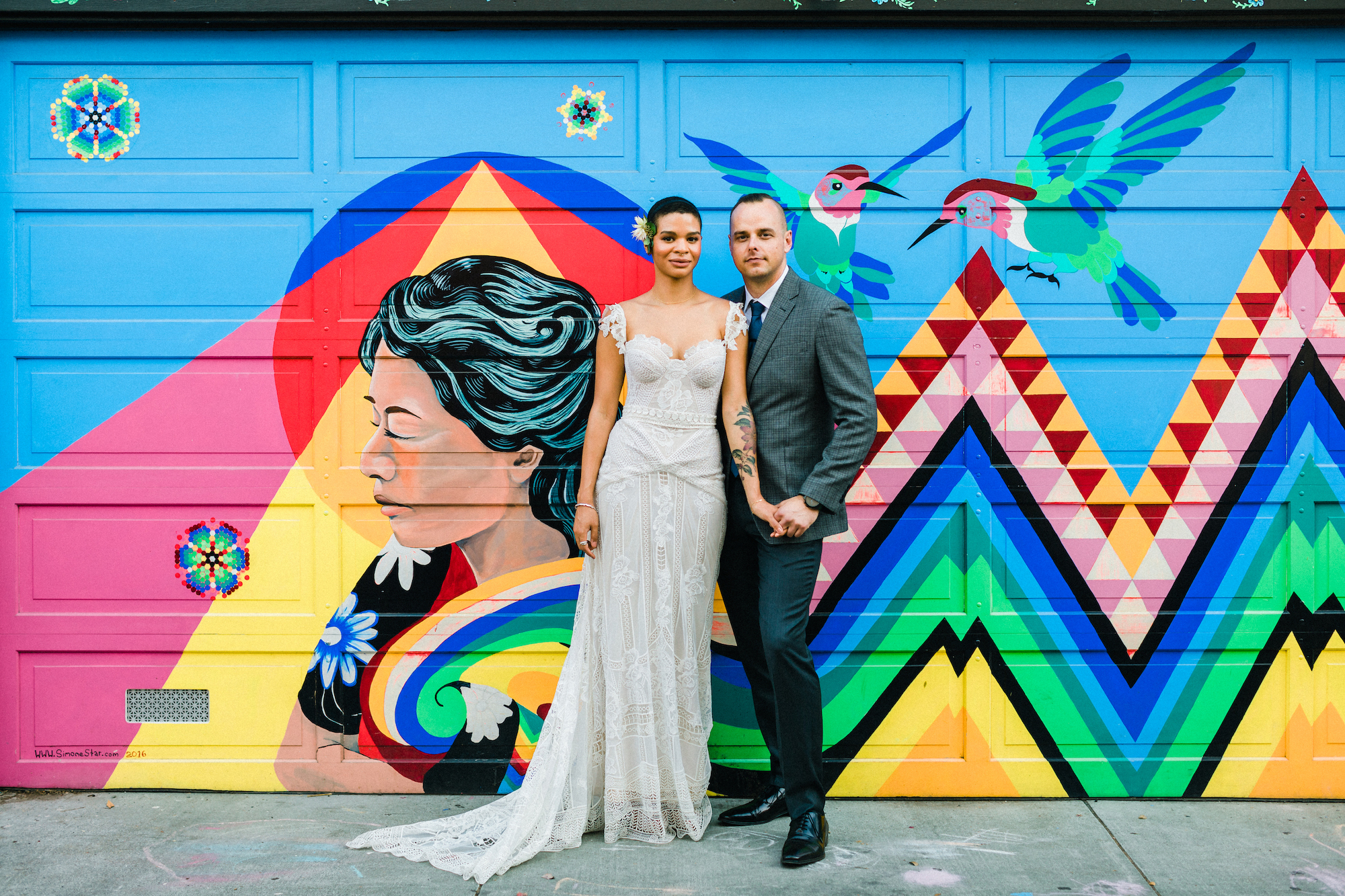 A wedding couple hold hands and pose in front of a garage door.