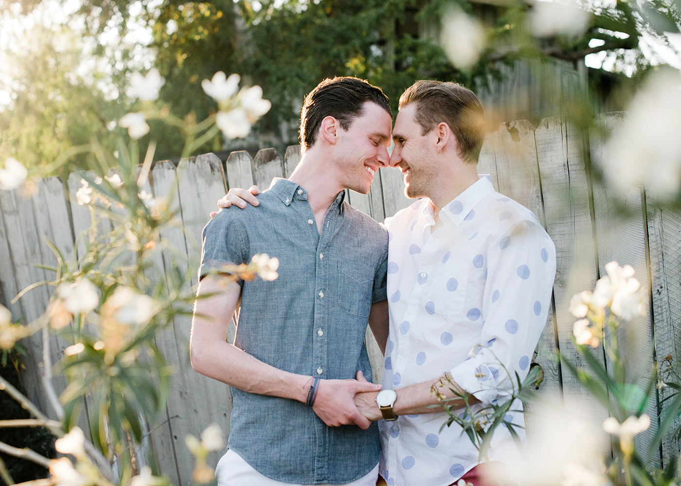 Two men hug and smile as seen through a field of flowers.