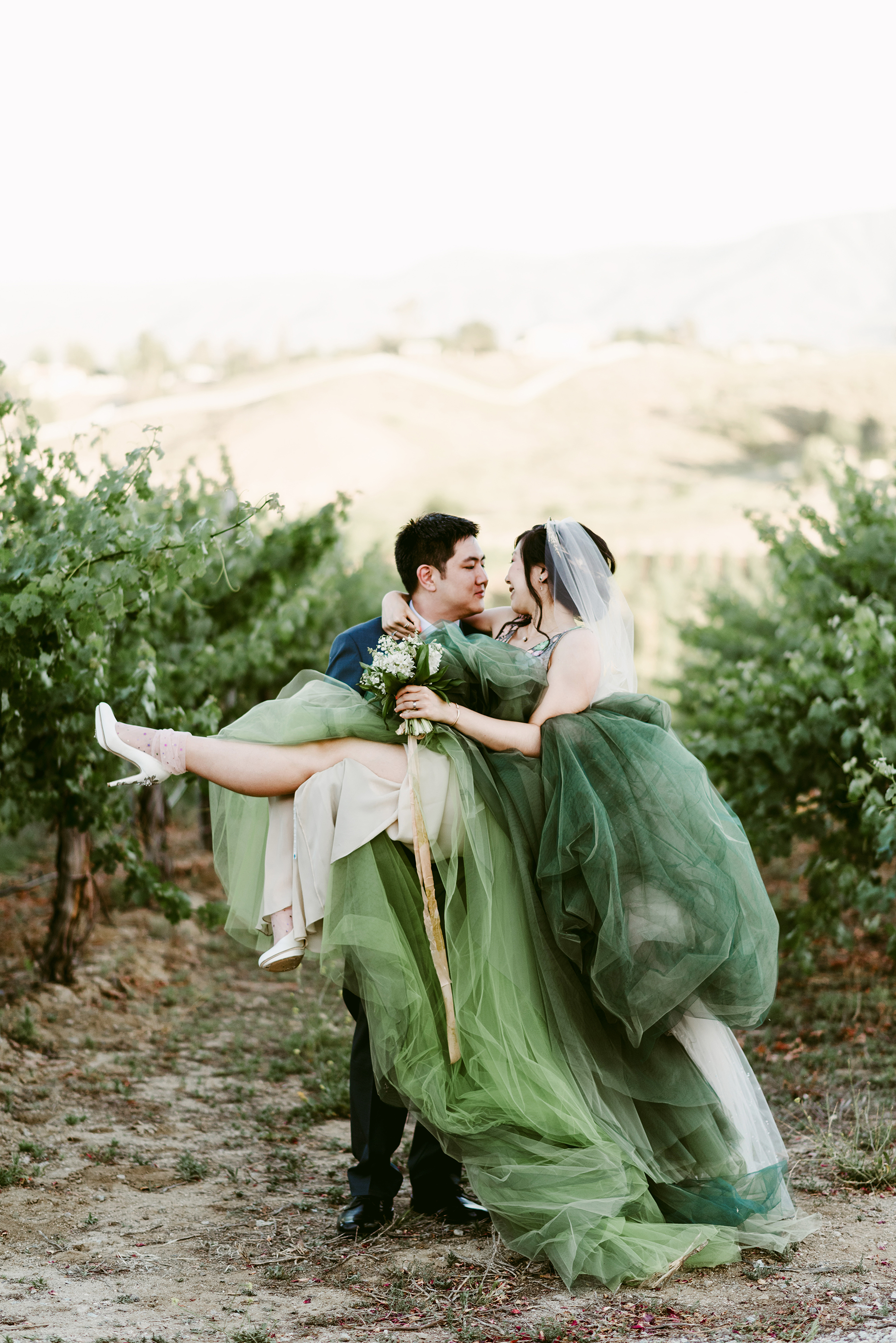 A man carries his bride as she wears a green wedding dress.