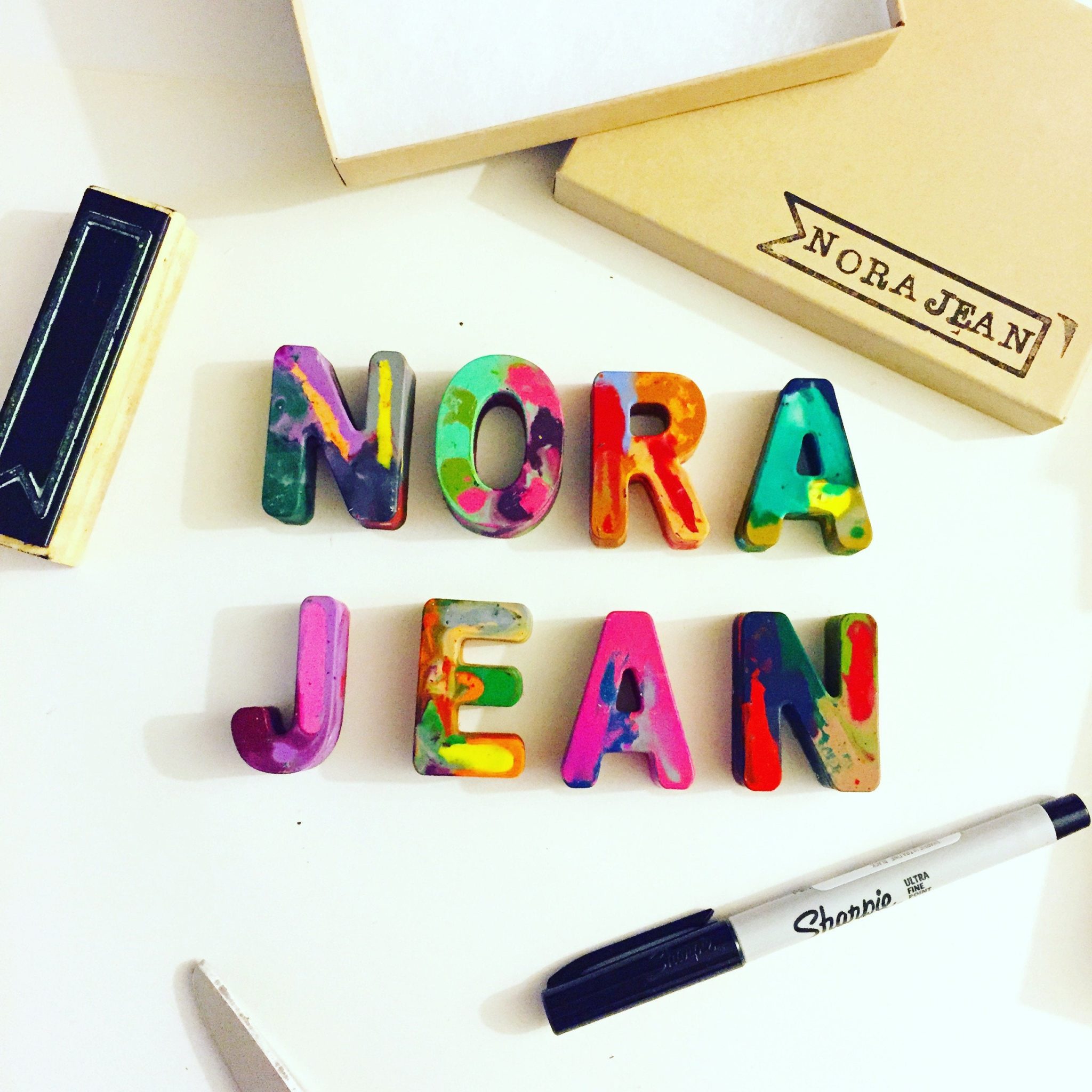 Colorful rainbow crayons in the shape of letters spelling out NORA JEAN.