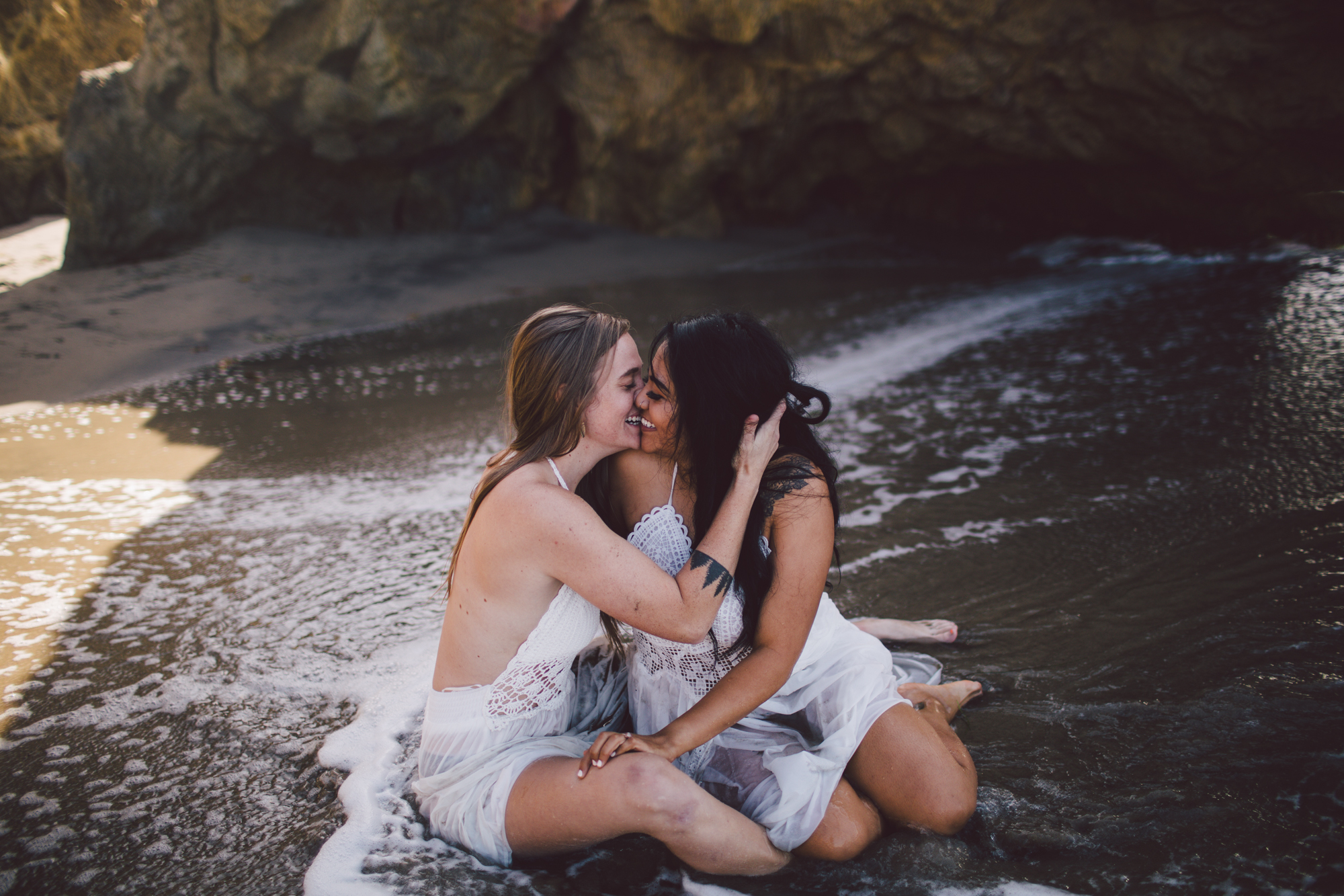 Two women kiss while on a beach.