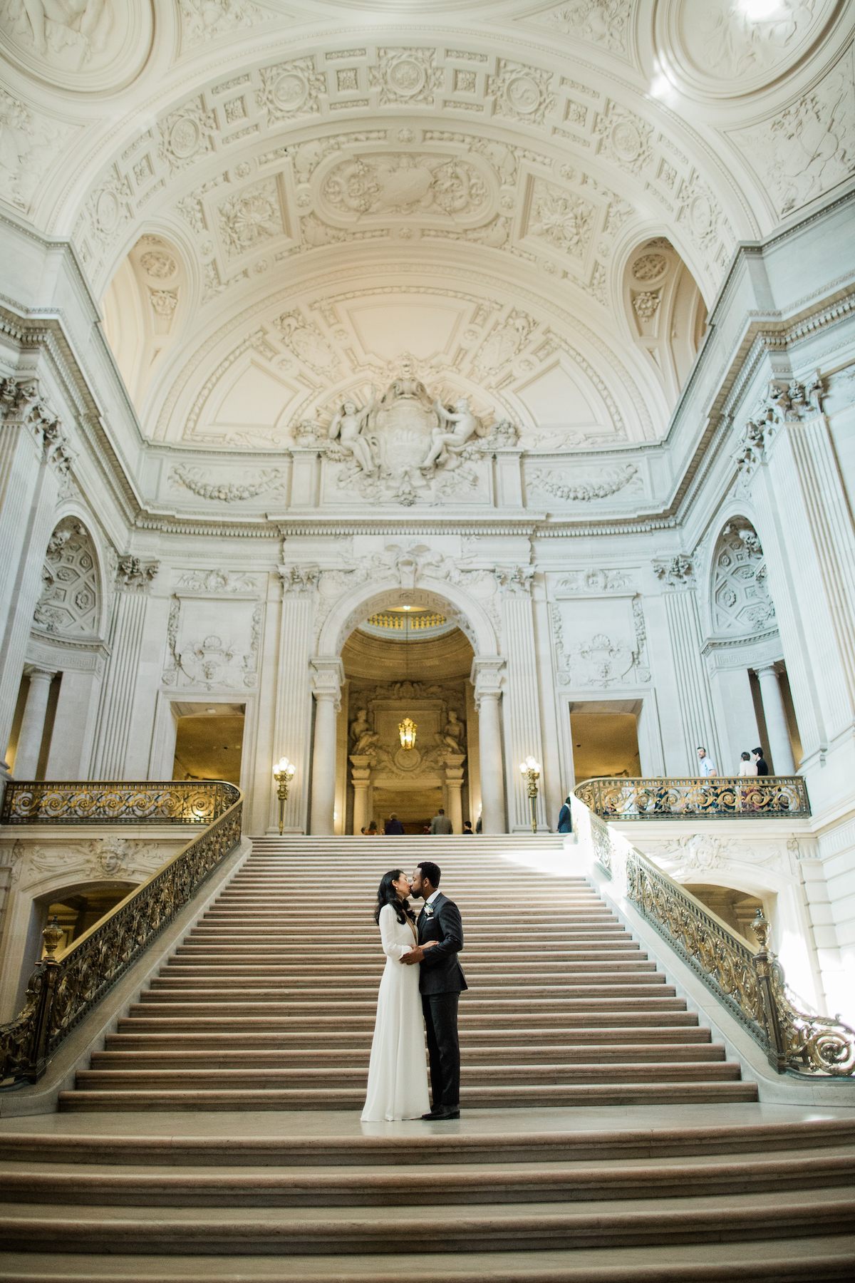 A wedding couple kiss while standing on steps in City Hall