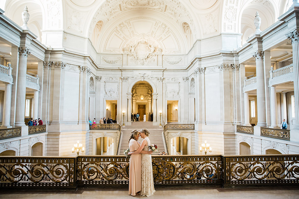 A wedding couple embrace while standing on the upper level of city hall.