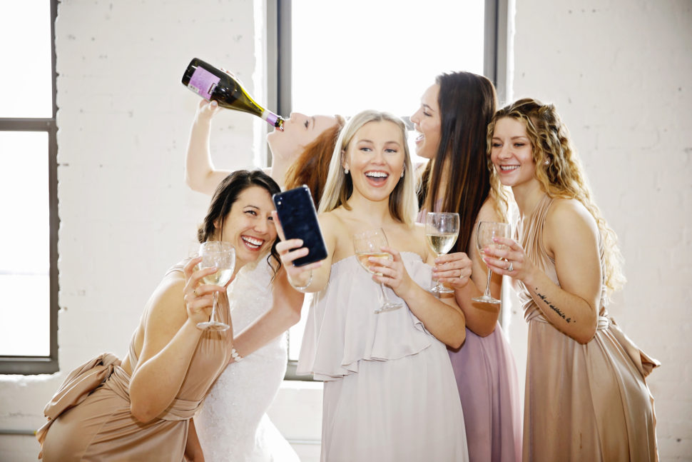 A group of women smile at someone taking a selfie while they drink champagne. 