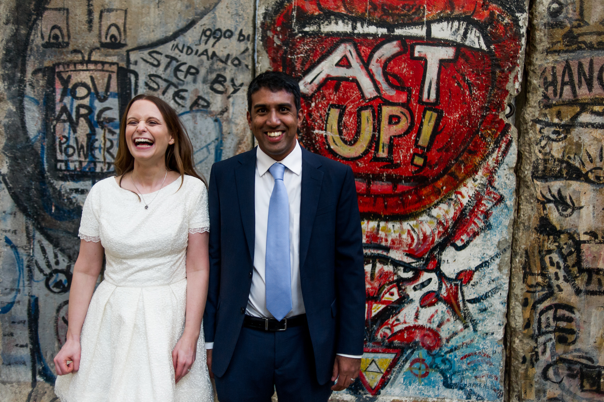 A wedding couple hold hands and smile while standing in front of a graffiti wall.