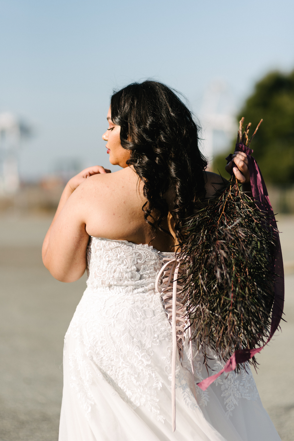 A woman holding a bouquet shows off the corset-style back of the Maggie Sottero wedding dress style 'Vanessa.'
