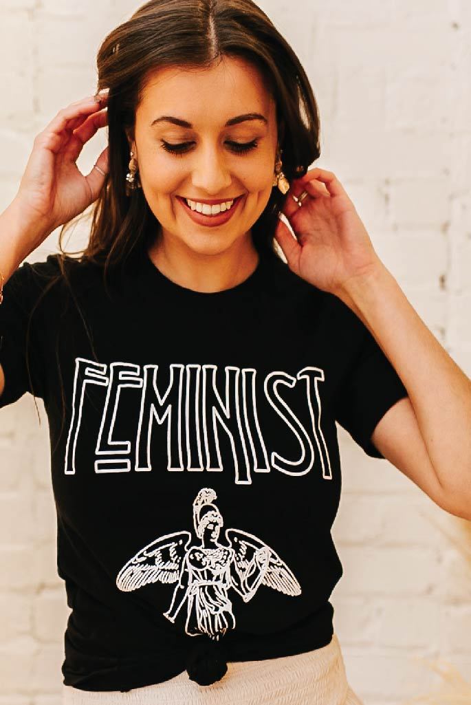 A woman wears a black shirt with the word Feminist printed on it.