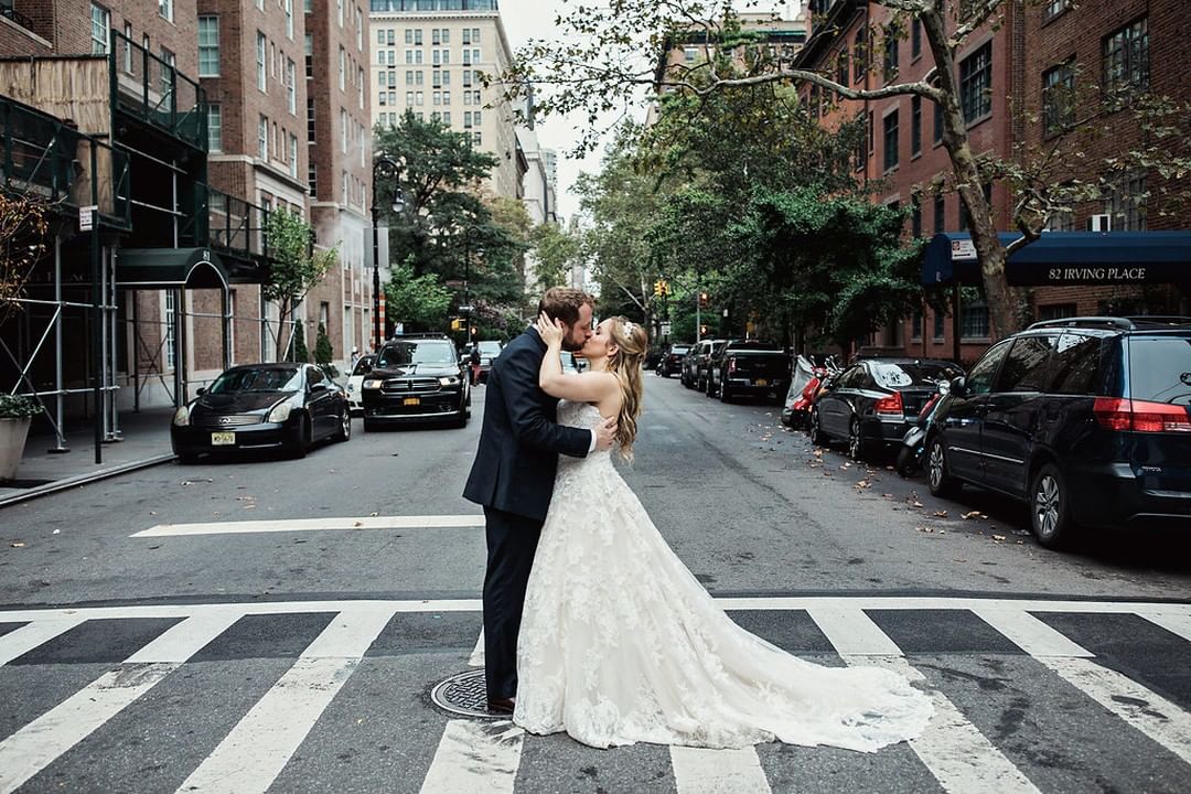 Bride and groom stand in the middle of a crosswalk of a NYC street lined with brownstone