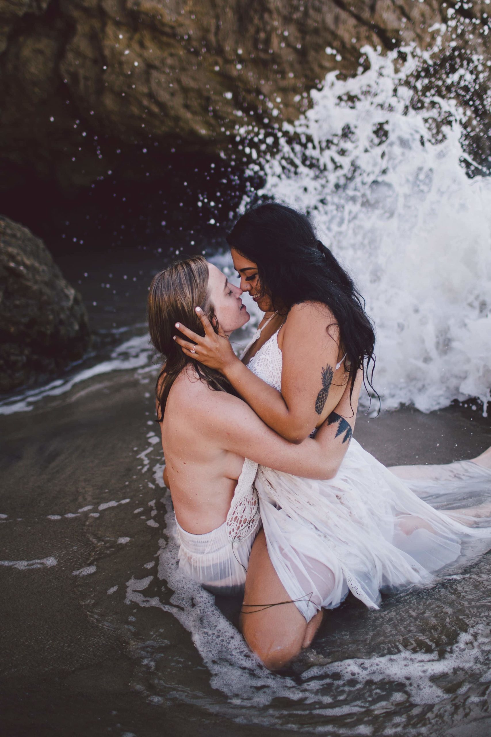 Two brides in white gowns kiss in a waterfall