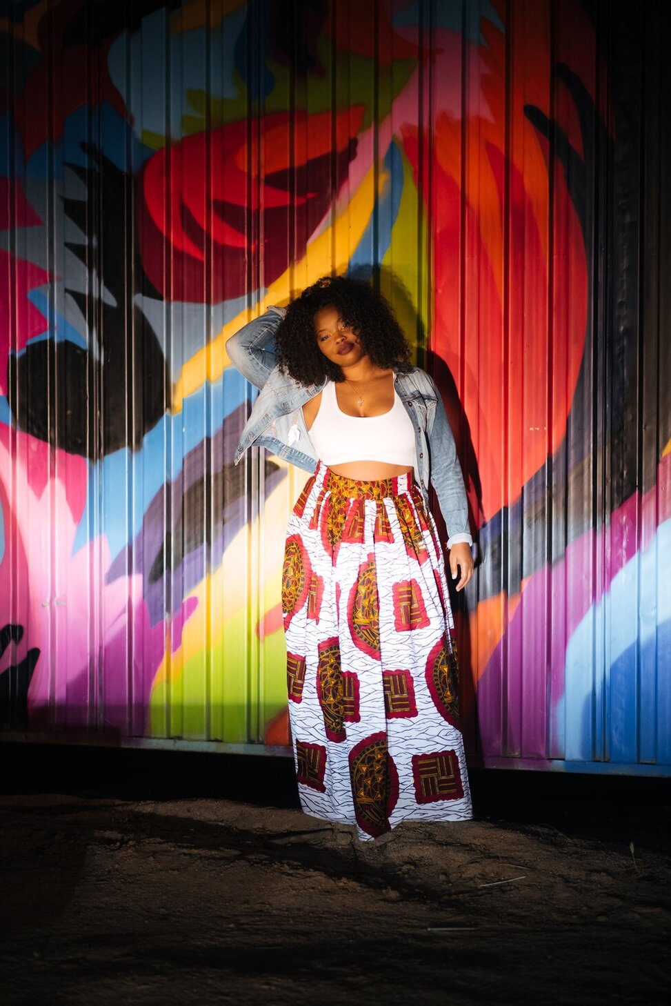 black woman leaning against a graffiti wall wearing a white top with printed pants