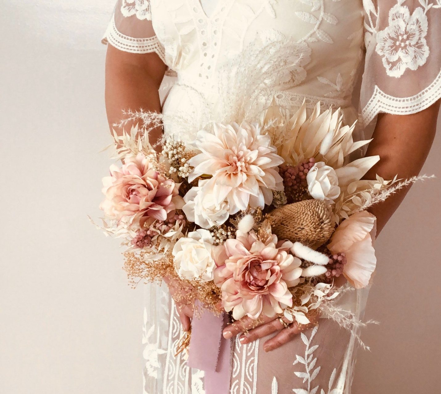 Woman in white dress holding faux and dried floral wedding bouquet