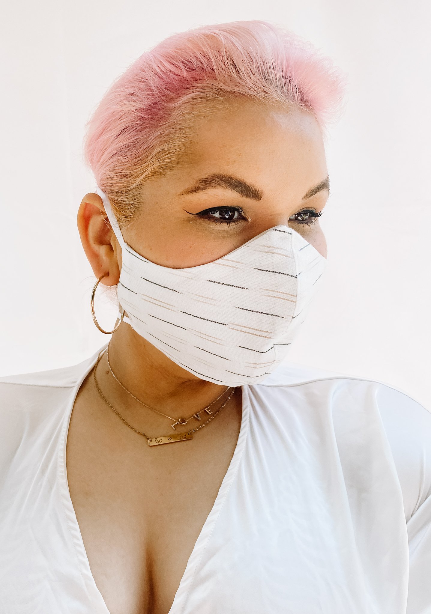 a woman with short pink hair wearing a white face mask with neutral color thin stripes