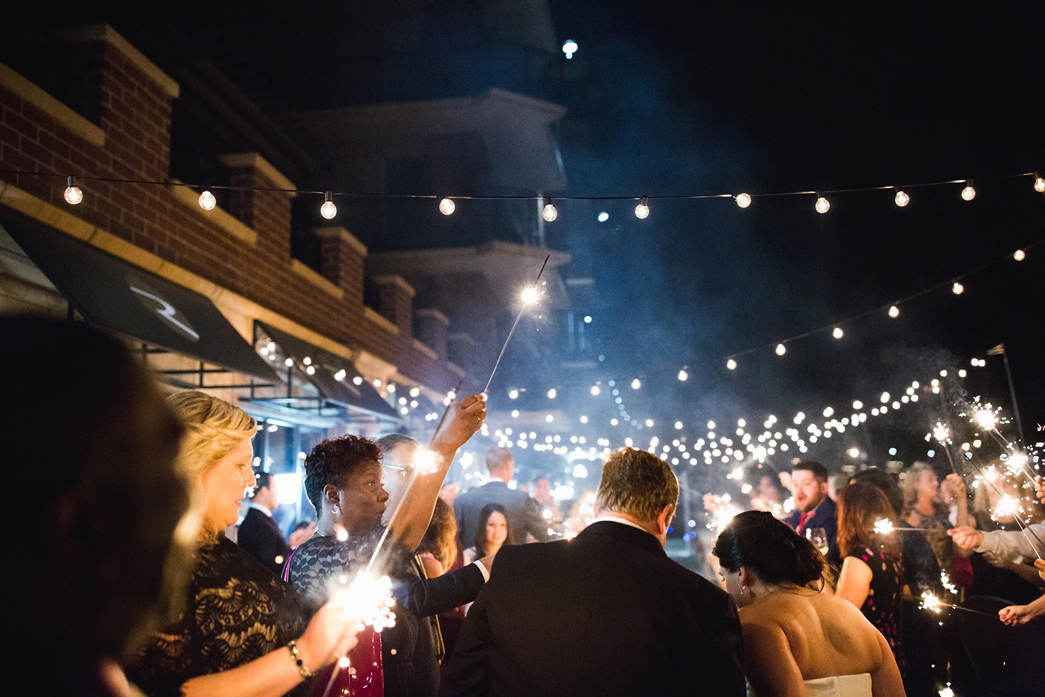 people with sparklers around bride and groom at wedding reception