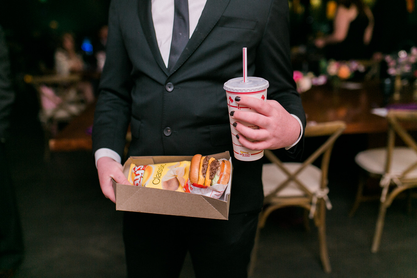 Person holding In-n-out burger meal in suit at wedding reception