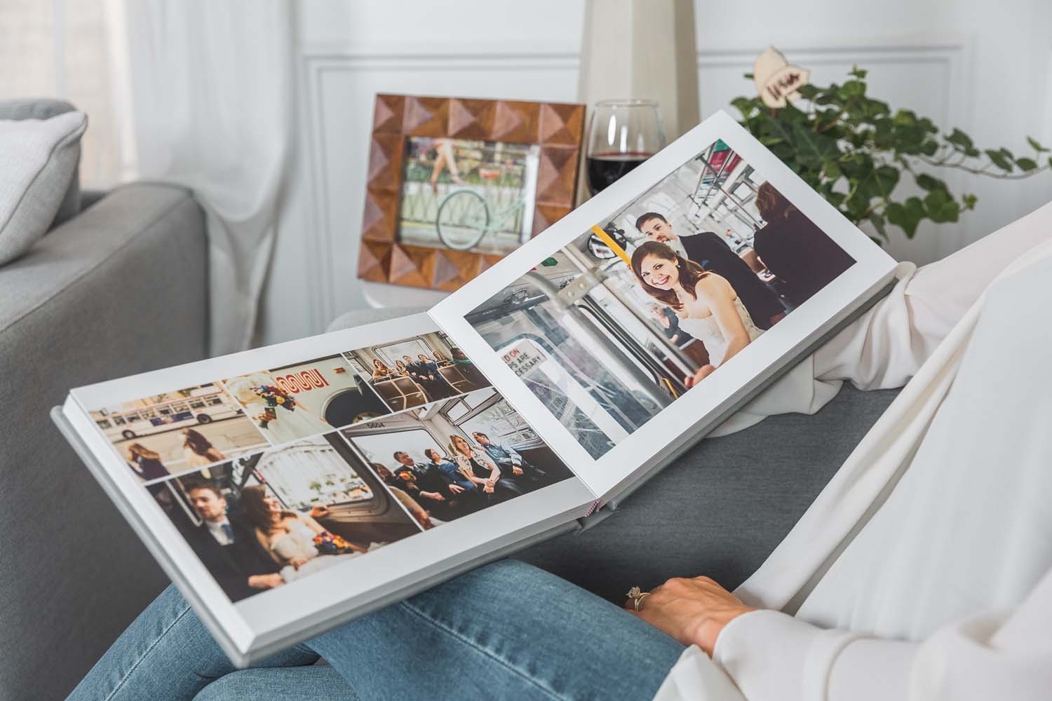 person sitting on a sofa with an Albums Remembered wedding album open on their lap showing a photo of a bride and groom standing in a bus