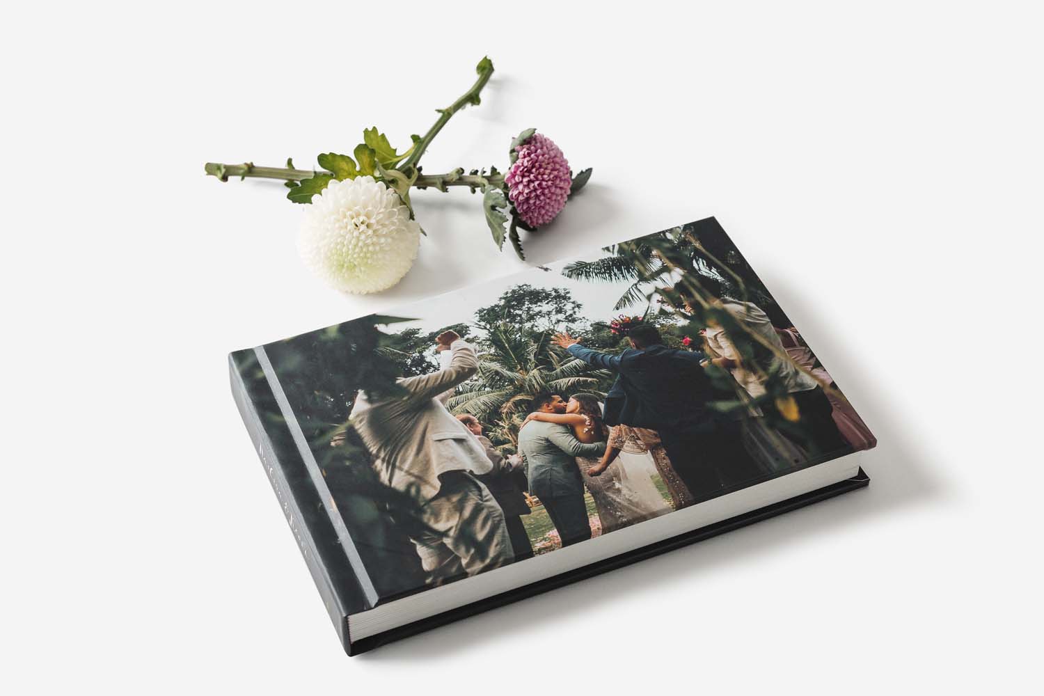 a white background with several flowers and an Albums Remembered wedding album with an image of a bride and groom kissing in a tropical location on the cover