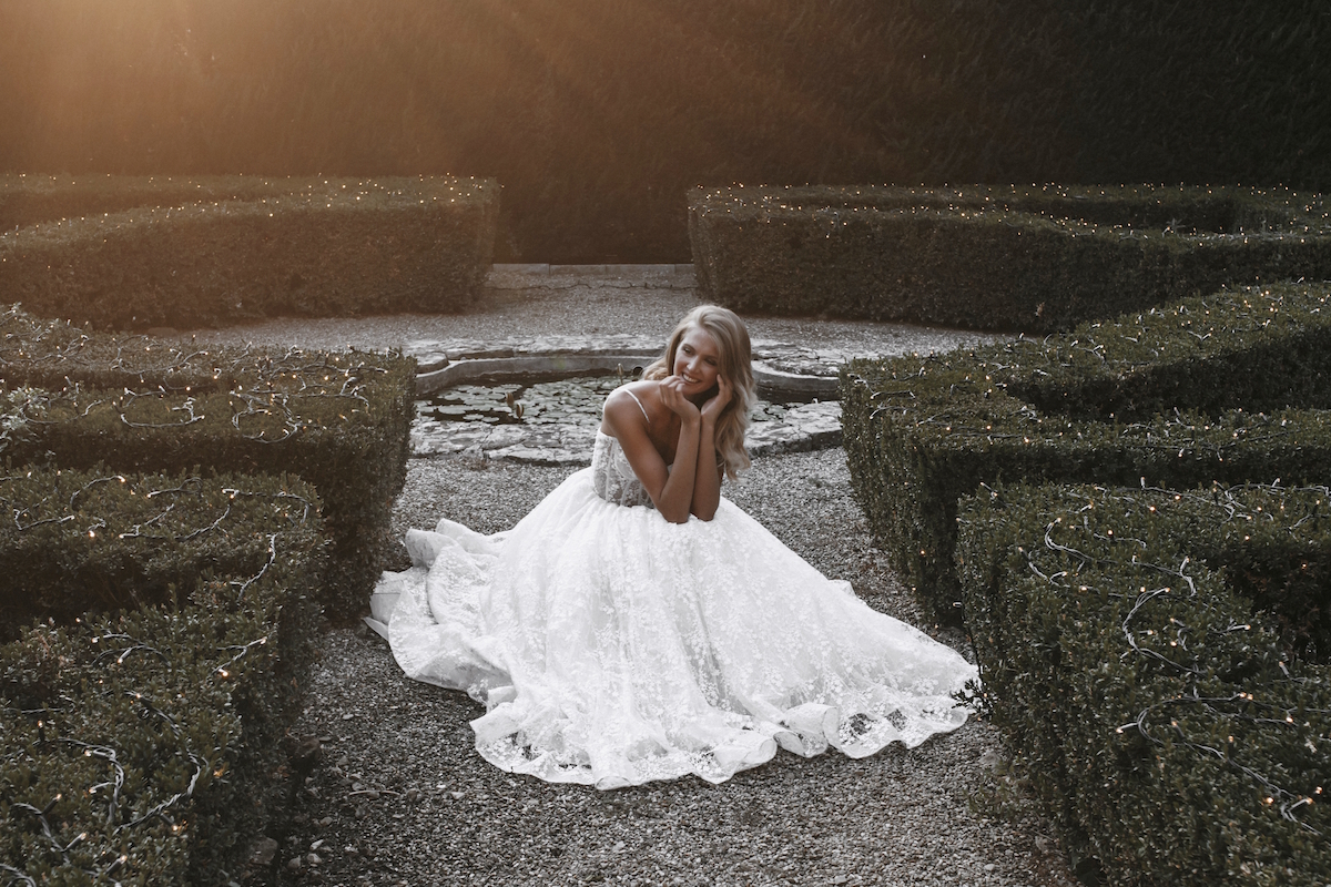 Woman in garden bent down wearing white Allure Bridals wedding dress 