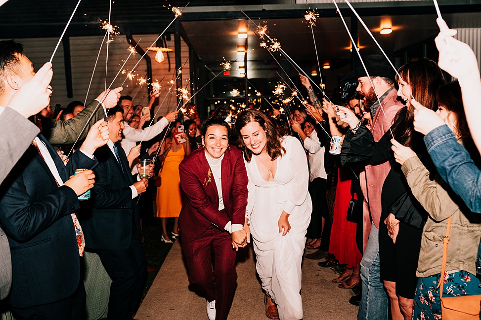 Two brides run through a tunnel of sparklers to a wedding entrance song